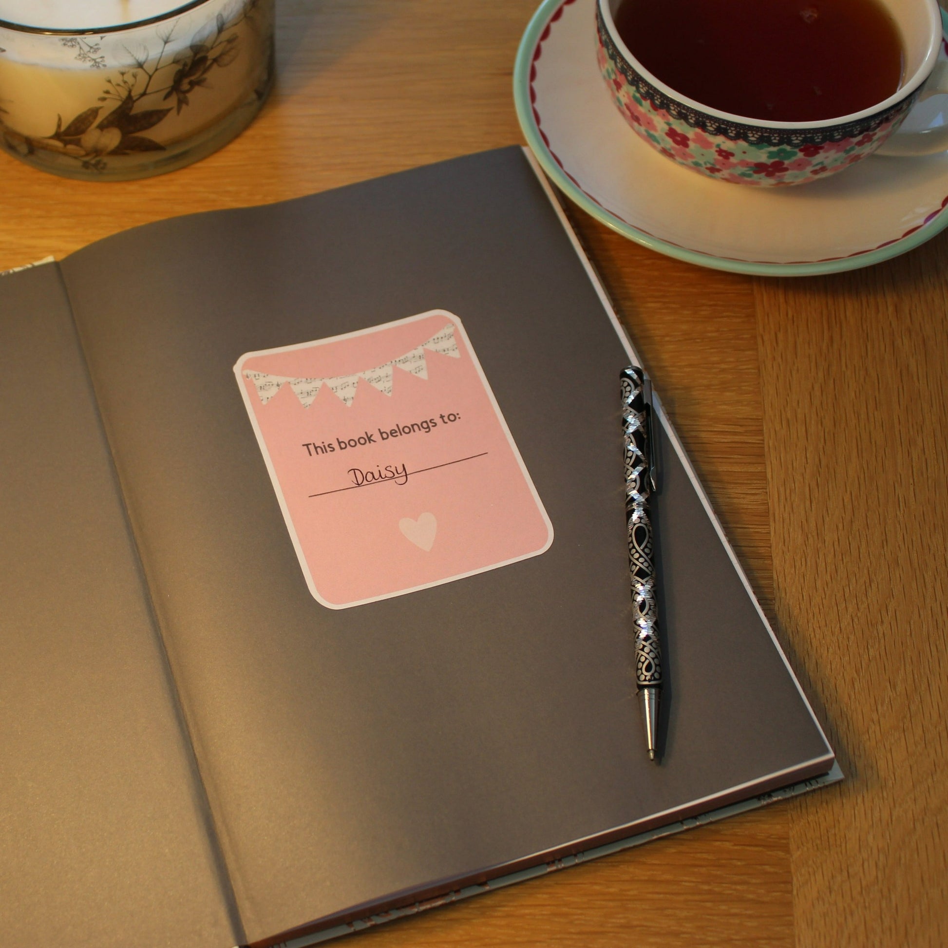 Pink bookplate with music bunting displayed in the front of a book. A cup of tea in the background